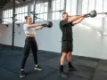 Kobieta i mężczyzna wykonują ćwiczenia z kettlebellami w siłowni.