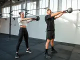 Kobieta i mężczyzna wykonują ćwiczenia z kettlebellami w siłowni.